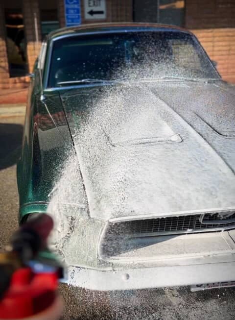 Foam being sprayed onto a green classic Ford Mustang